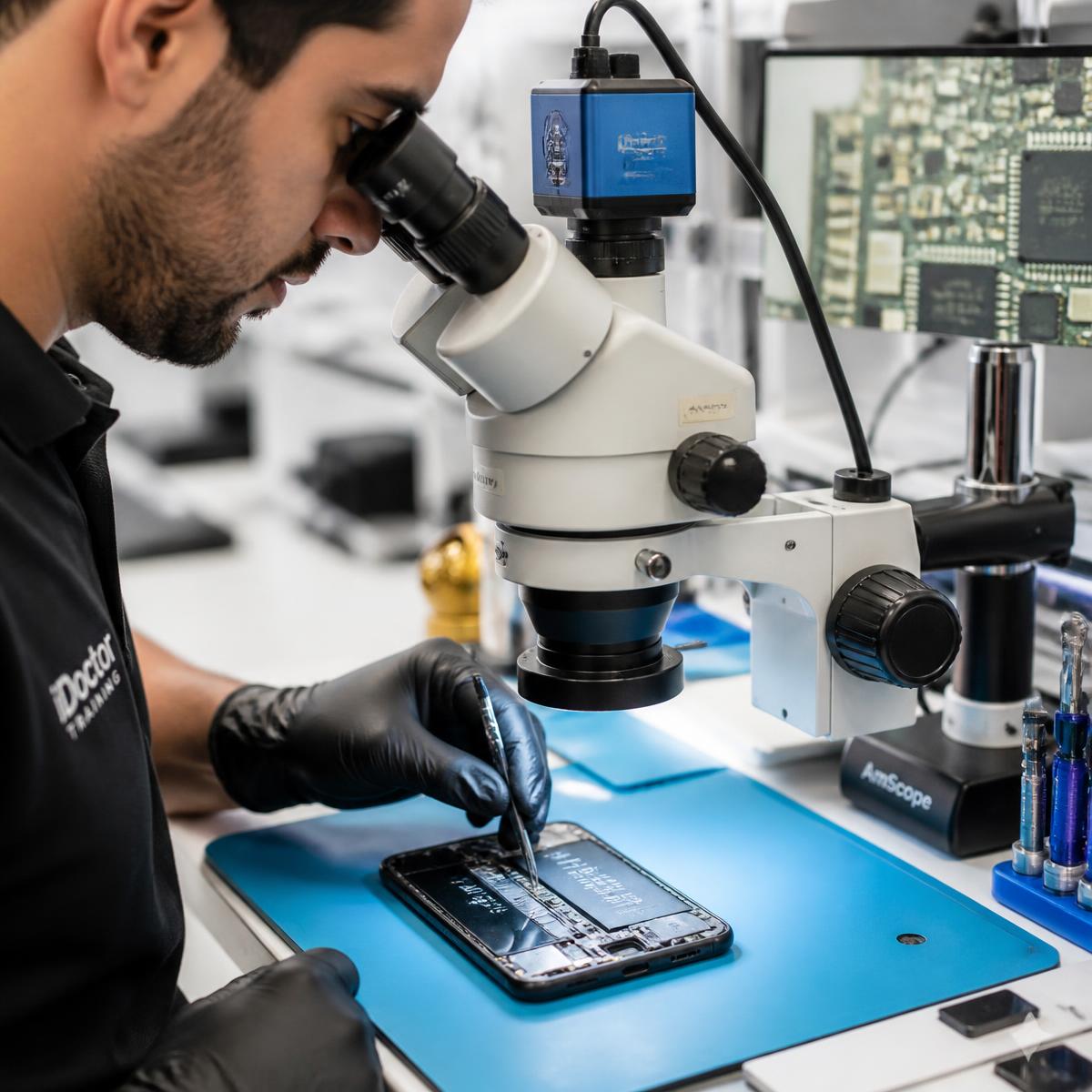 Technician repairing a smartphone under a digital microscope in our Katy training lab